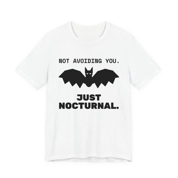 White t-shirt printed in dark ink with “Not Avoiding You.” above a bat with wings spread, then “Just Nocturnal.”