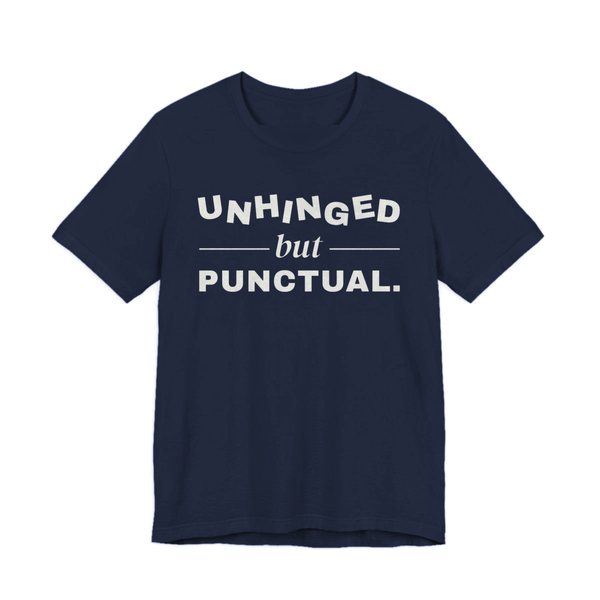 Navy t-shirt printed in off-white ink with “Unhinged” in wobbly capitals, a calm italic “but”, and “Punctual.” squared away underneath